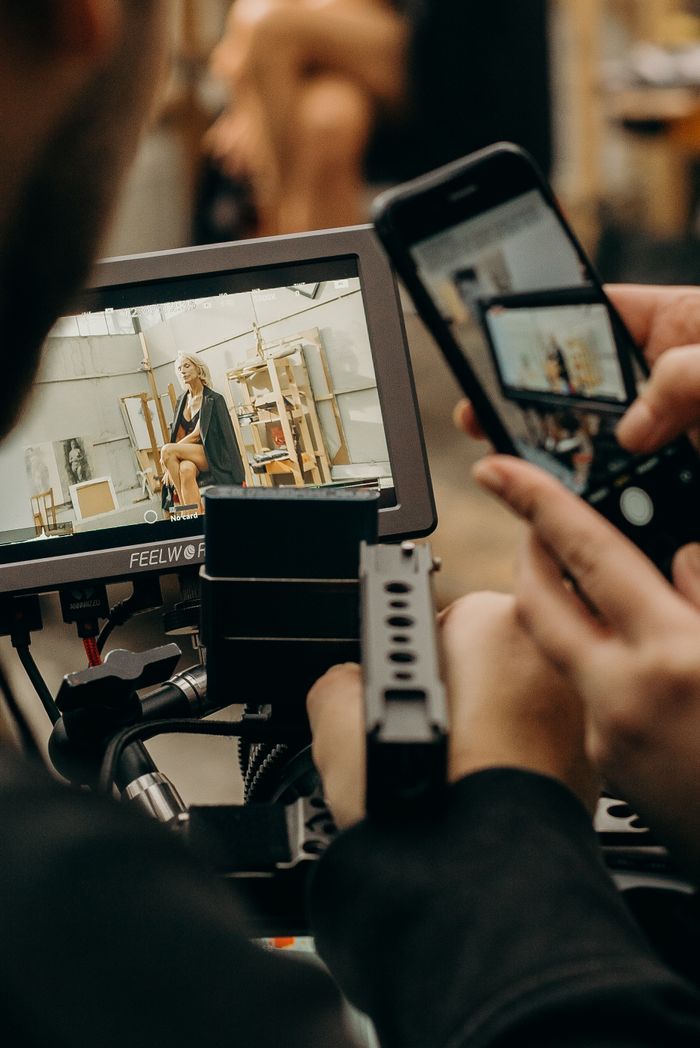 Home A photographer captures a video on a smartphone and monitor inside a studio setting.